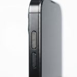 A macro studio shot focusing on the titanium edge and action button of the Apple iPhone 17 Pro in Black Titanium. The li